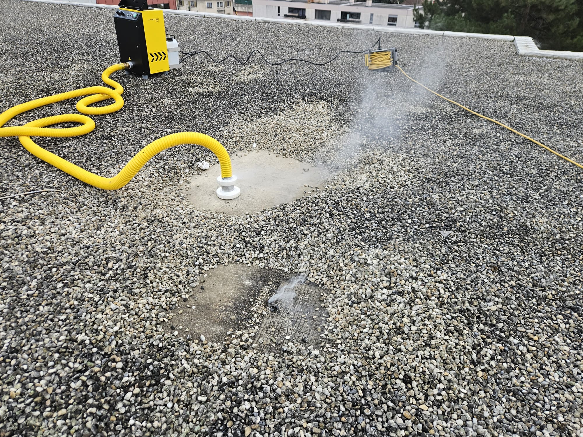 Test d'étanchéité au fumigène sur une toiture terrasse gravillonnée pour localiser une infiltration d'eau.