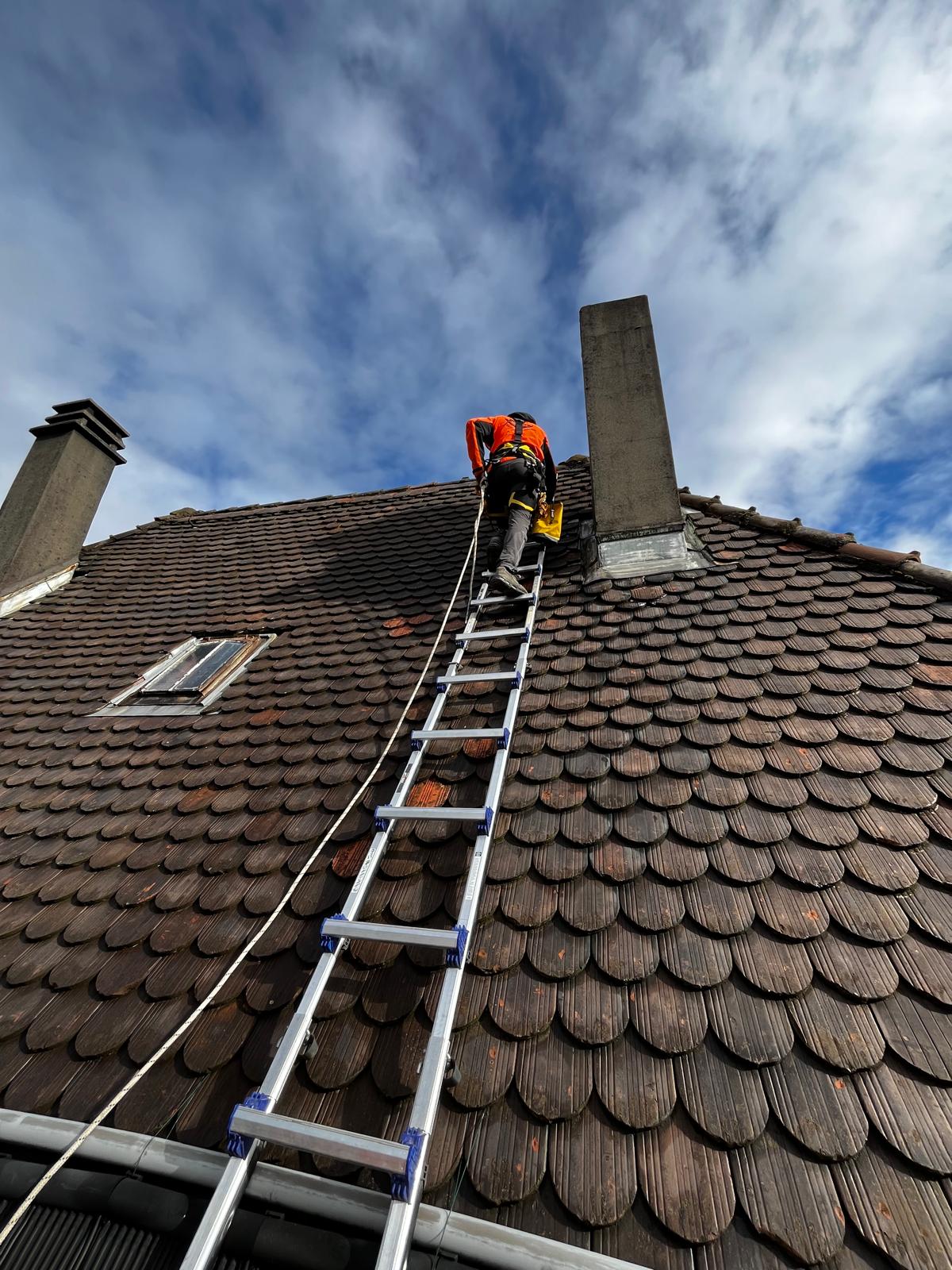 Cordiste d'Alp'In Services montant sur une échelle de toit pour l'entretien et le nettoyage d'une toiture en tuiles.