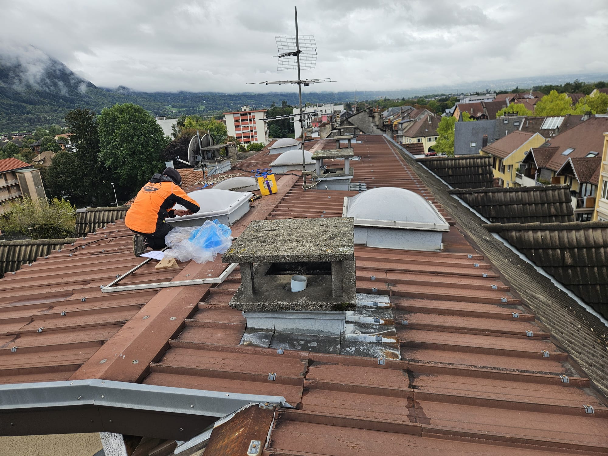 Technicien en intervention de maintenance sur une toiture terrasse avec lanterneaux, illustrant la capacité d'adaptation pour les syndics et entreprises.