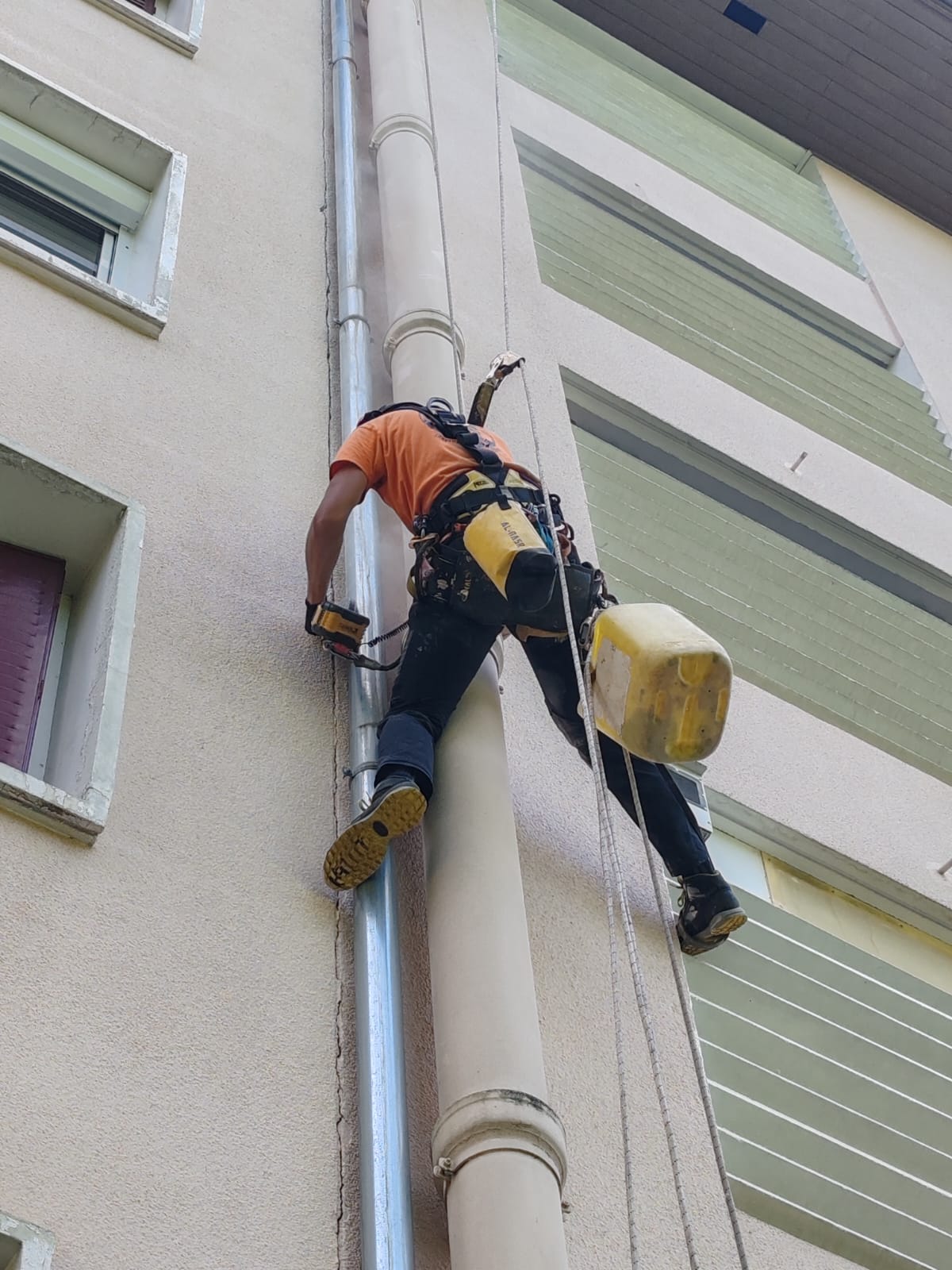 Technicien cordiste effectuant une réparation de précision sur une descente d'eau pluviale, illustrant le savoir-faire technique et la qualité des finitions.