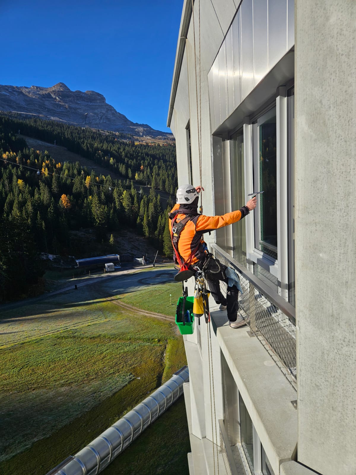 Cordiste appliquant une méthode de nettoyage douce et manuelle sur les vitres d'un immeuble en station de montagne, préservant les surfaces fragiles.