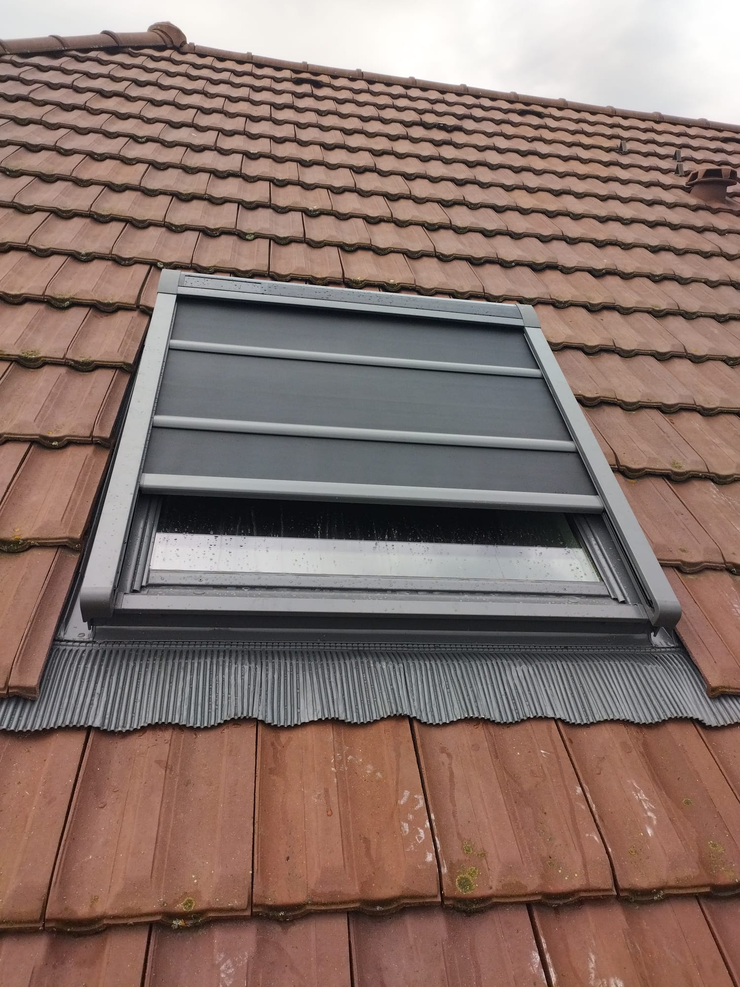 Installation d'une fenêtre de toit Velux avec volet roulant extérieur motorisé sur une toiture en tuiles, avec étanchéité refaite à neuf.