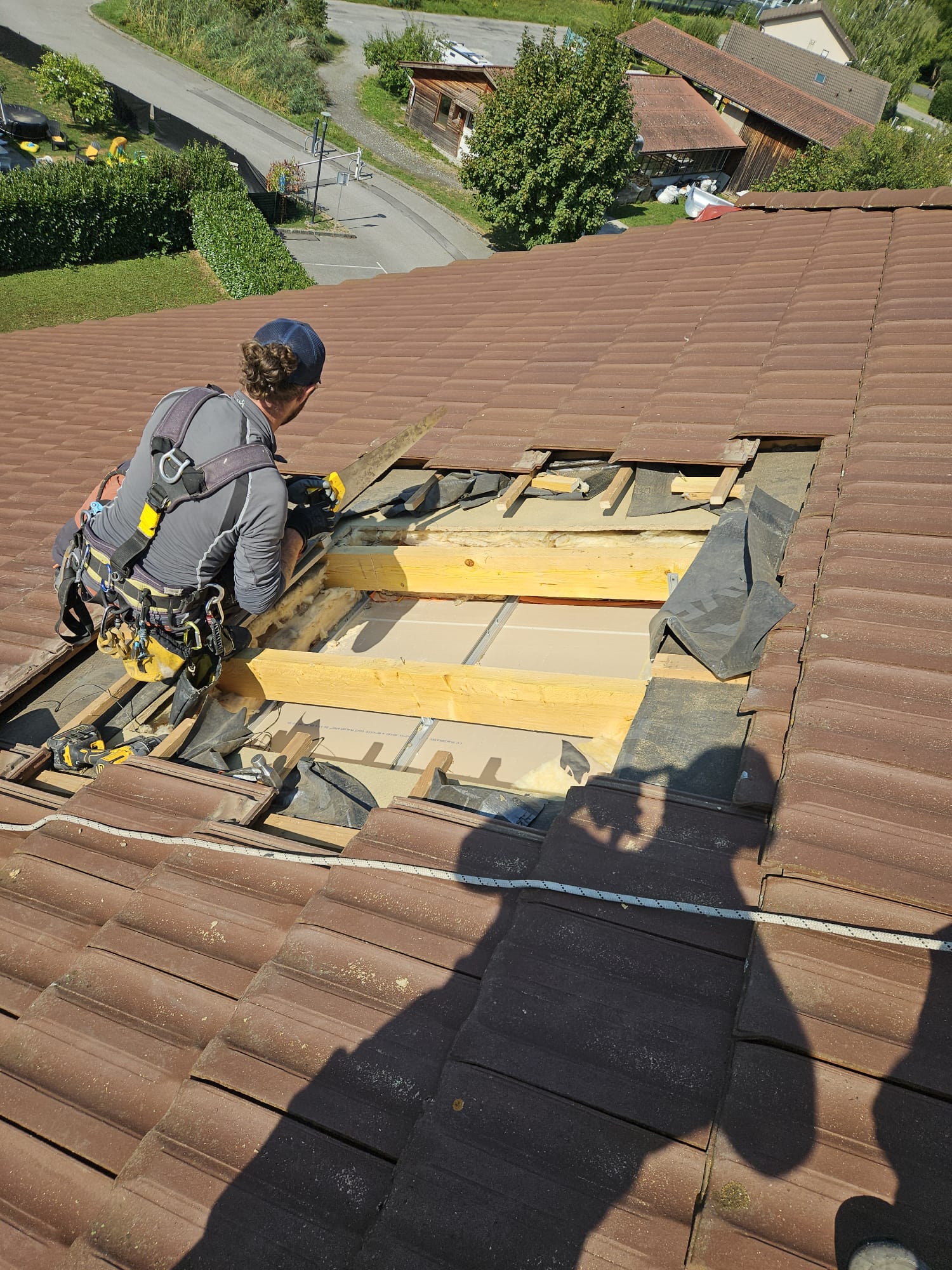 Technicien cordiste réalisant une ouverture dans une toiture en tuiles pour poser un Velux, illustrant l'intervention agile sans échafaudage.